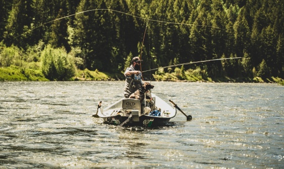 Man fishing in river from a boat with a dog