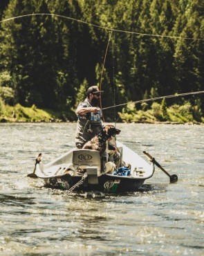 Man fishing in river from a boat with a dog